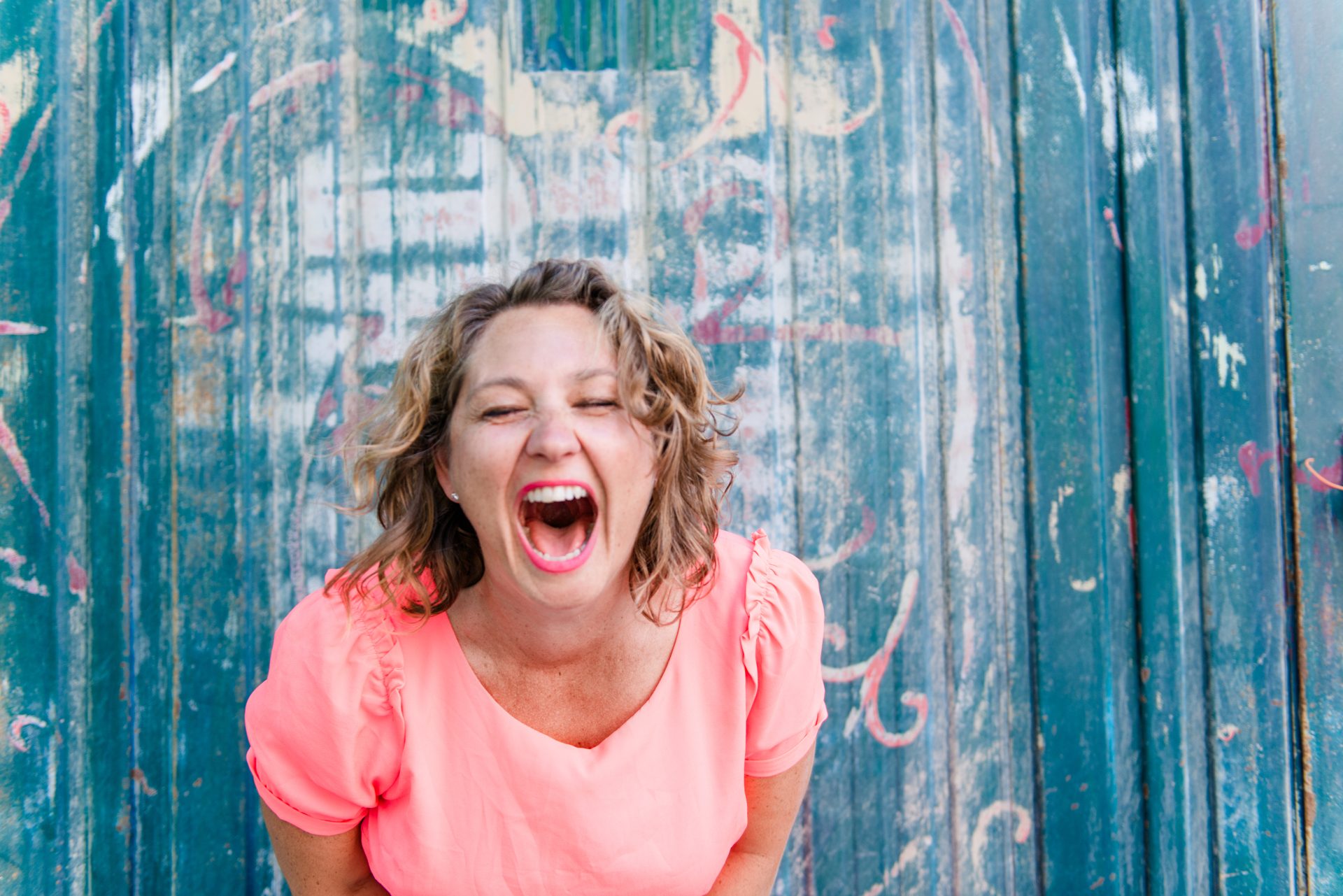 Natalie laughing wholeheartedly in front of a weathered teal door